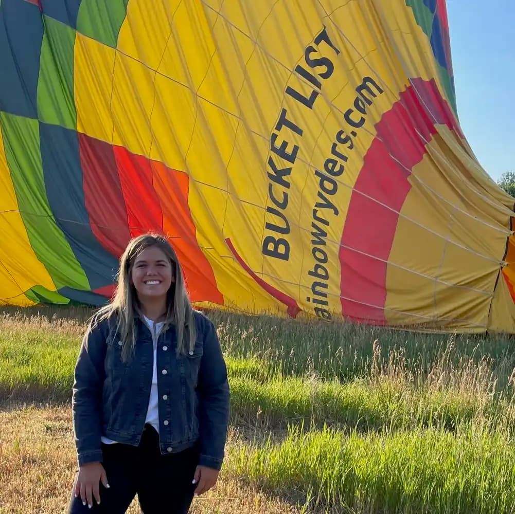 Nicole smiling in a field next to a colorful hot air balloon