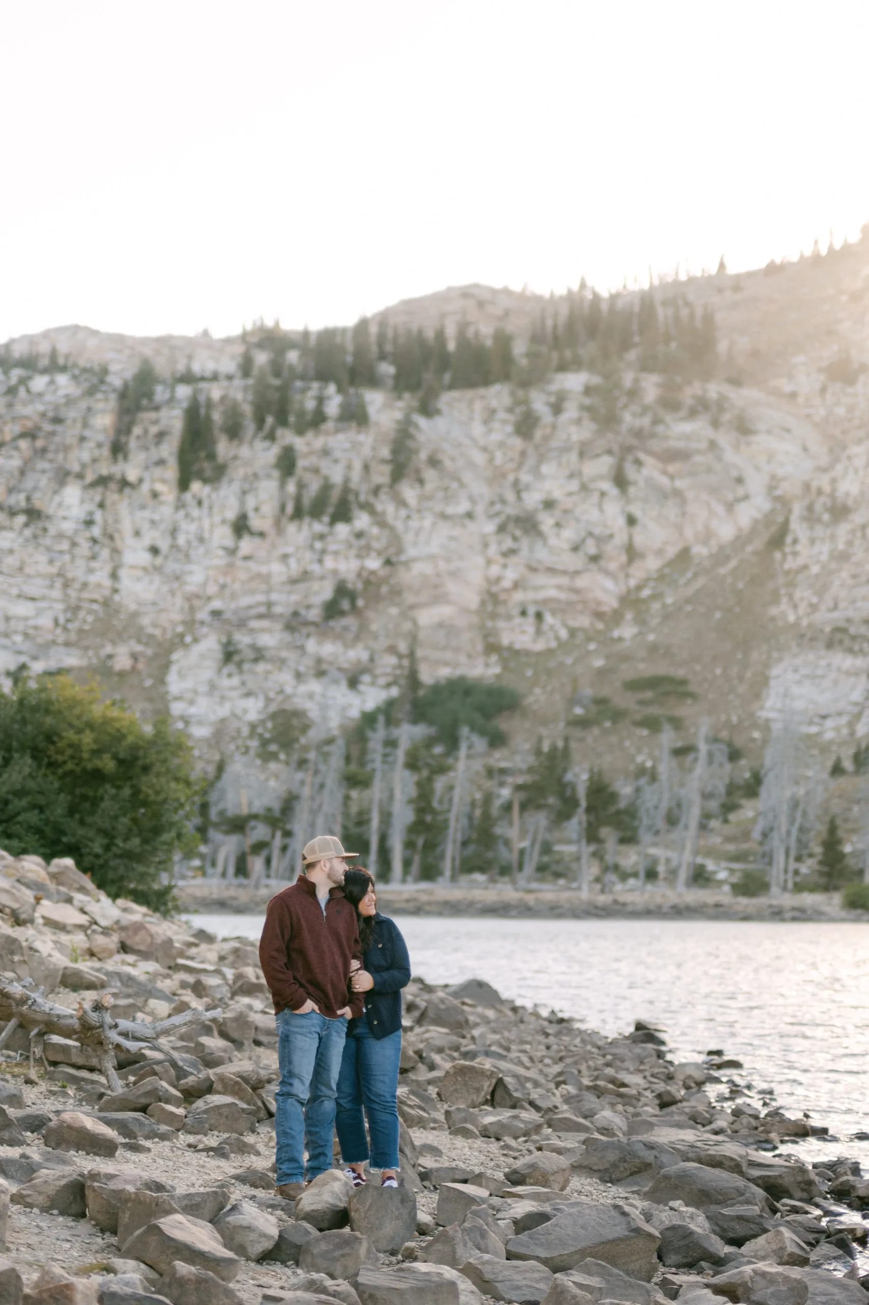 Craig and Nicole standing by the water with sunlit mountains in the background